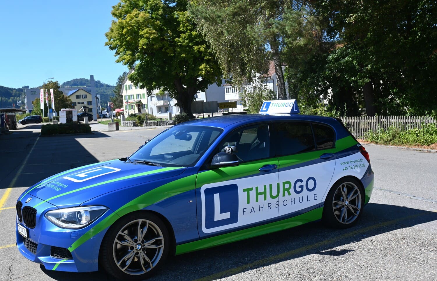 Fahrschulauto der Thurgo Fahrschule beim Bahnhof Eschlikon TG vor Wohnhäusern und Bäumen