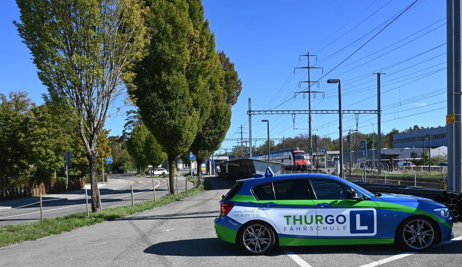 Fahrschulauto der Thurgo Fahrschule beim Bahnhof Märstetten mit SBB-Zug und Bahngleisen im Hintergrund