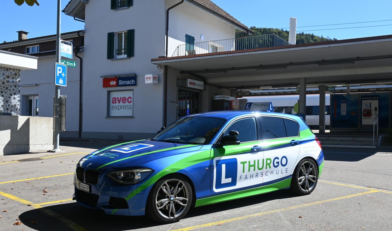 Fahrschulauto der Thurgo Fahrschule vor dem Bahnhof Sirnach mit Bahnhofsgebäude im Hintergrund