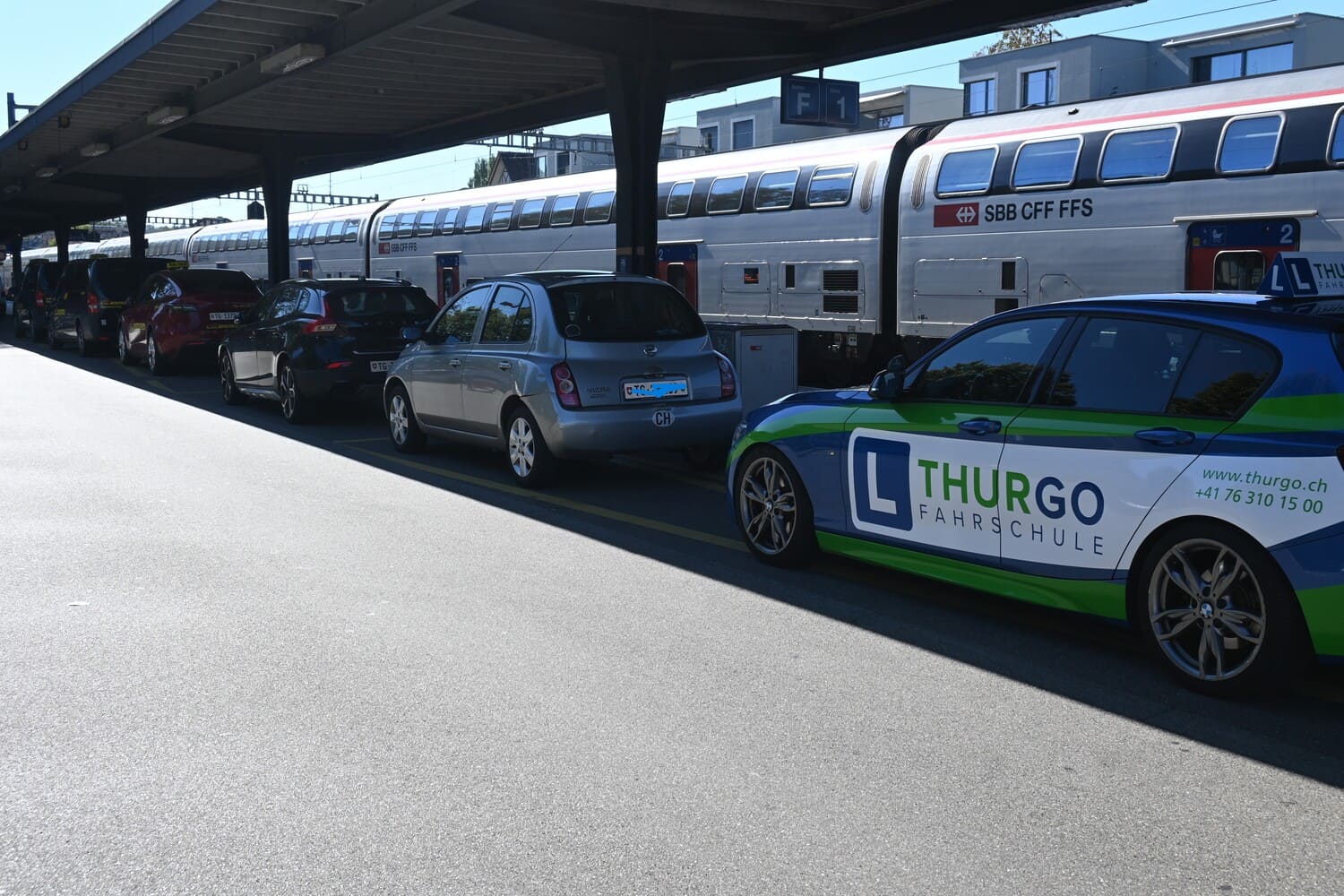 Fahrschulauto der Thurgo Fahrschule beim Frauenfeld Bahnhof neben einem SBB-Doppelstockzug