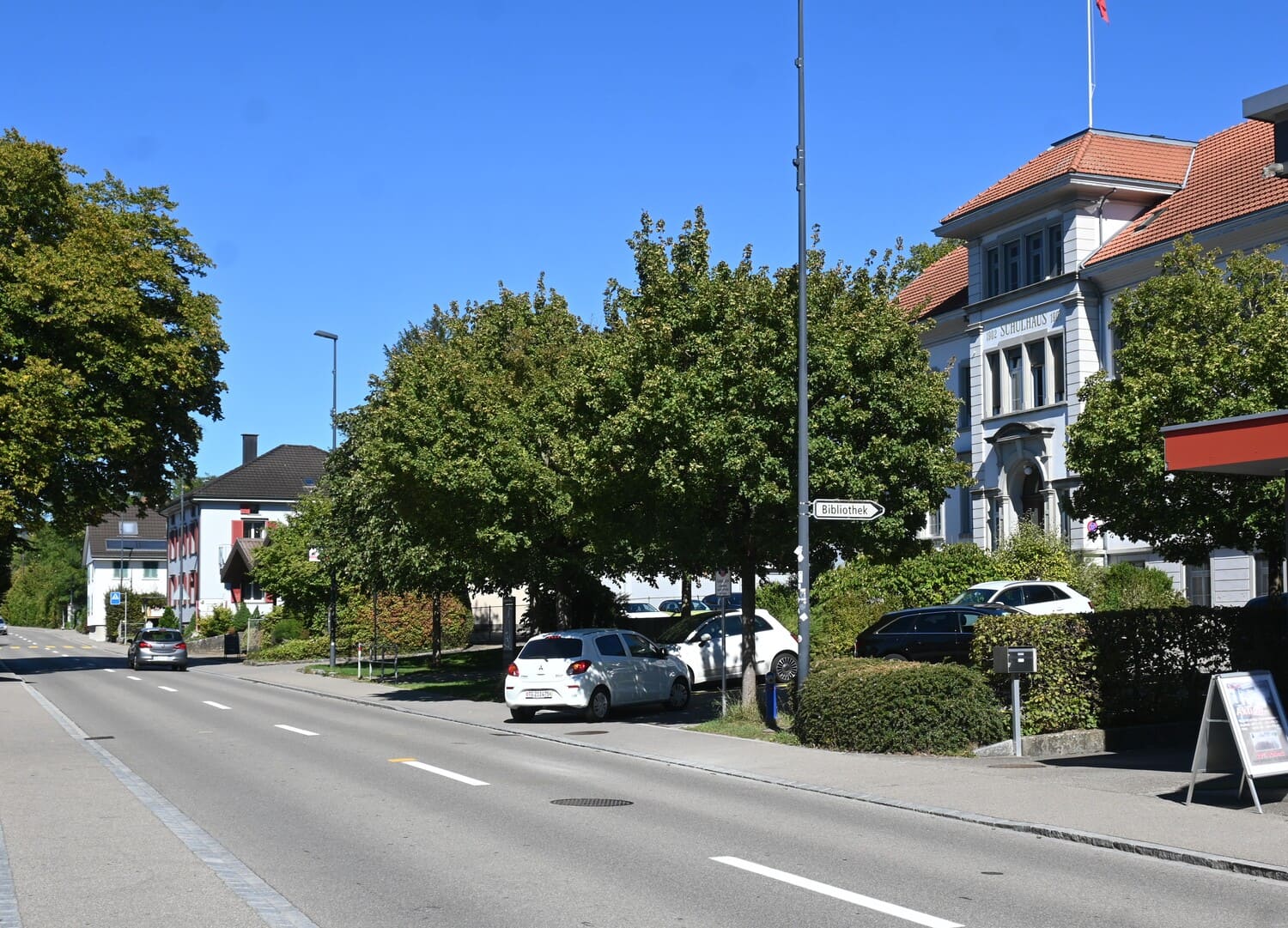Schulhaus Wängi an einer von Bäumen gesäumten Strasse mit parkierten Autos – Fahrschule in Wängi