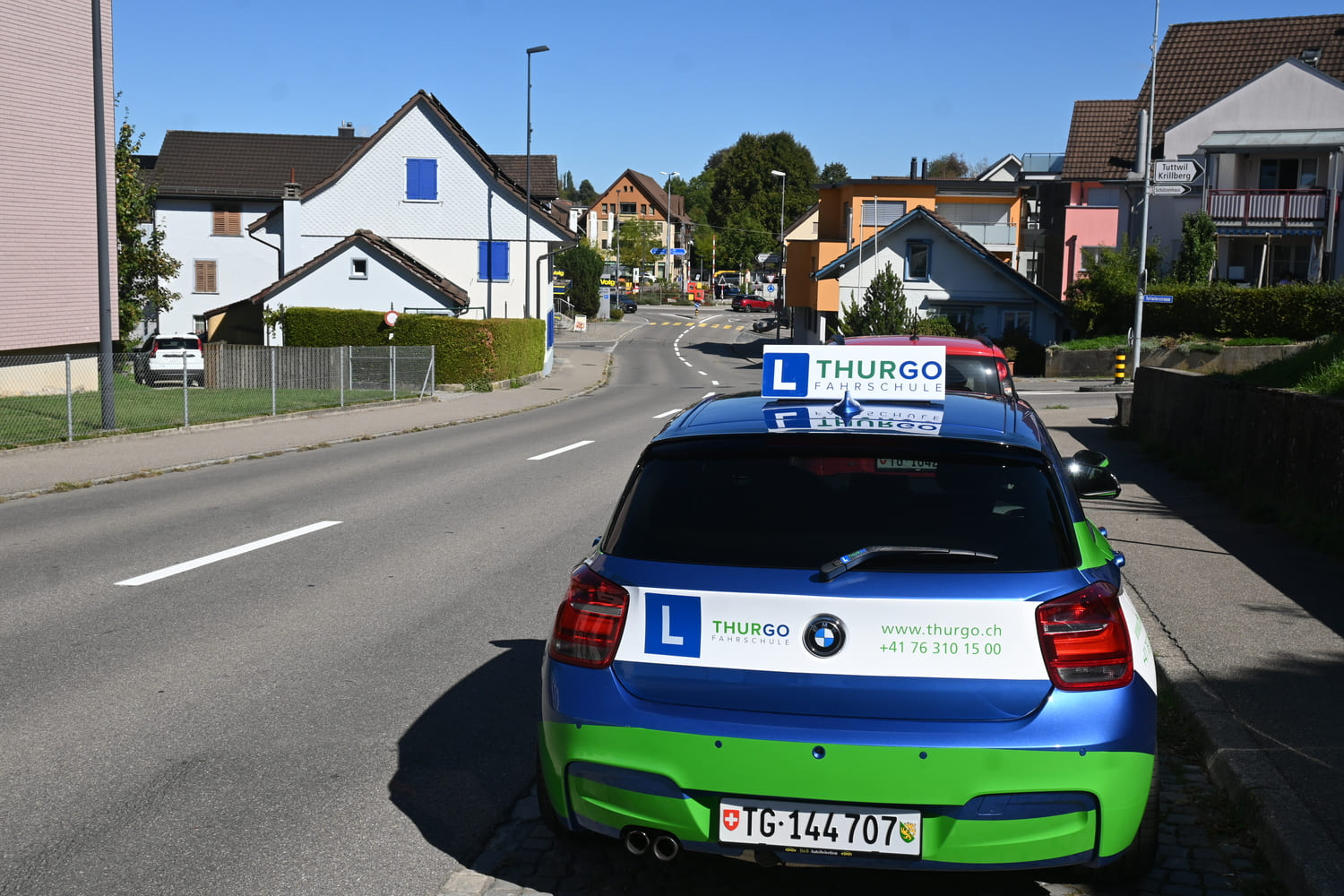Fahrschulauto der Thurgo Fahrschule in Wängi an einer Wohnstrasse mit Wegweisern Richtung Tuttwil und Krillberg