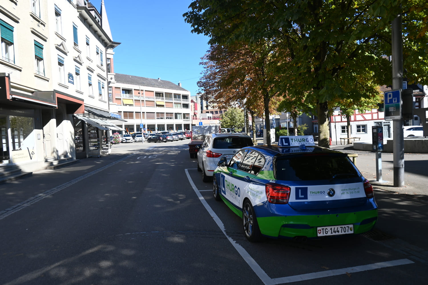 Fahrschulauto der Thurgo Fahrschule am Marktplatz Weinfelden mit parkierten Fahrzeugen und Gebäuden im Zentrum